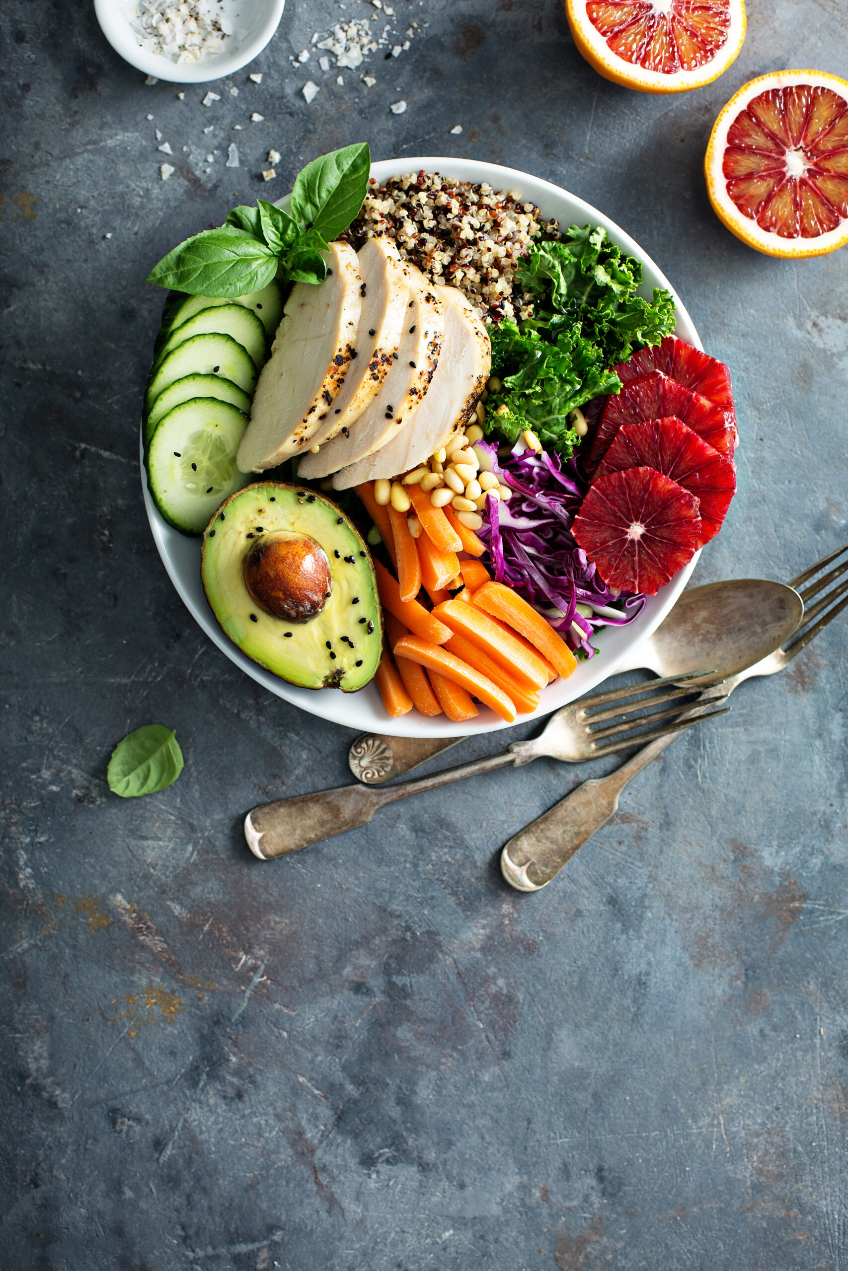 healthy lunch in a bowl with grilled chicken, avocado, fruit, cucumbers, carrots