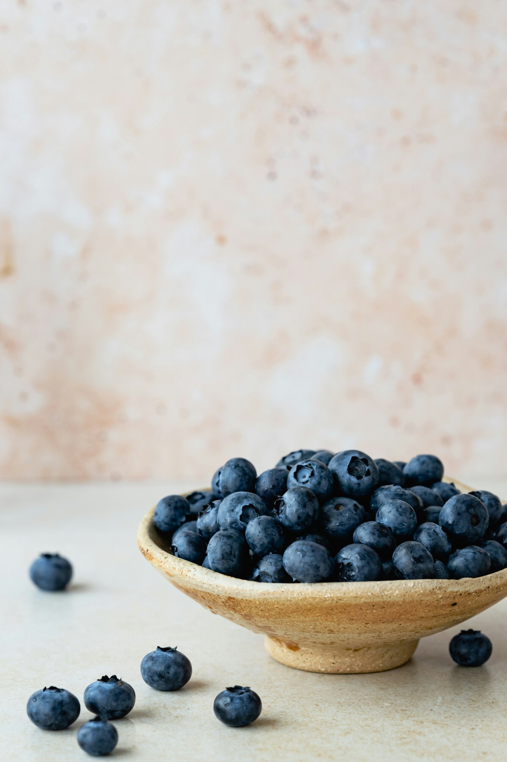 Bowl of blueberries with a few on the tabletop with a light beige background