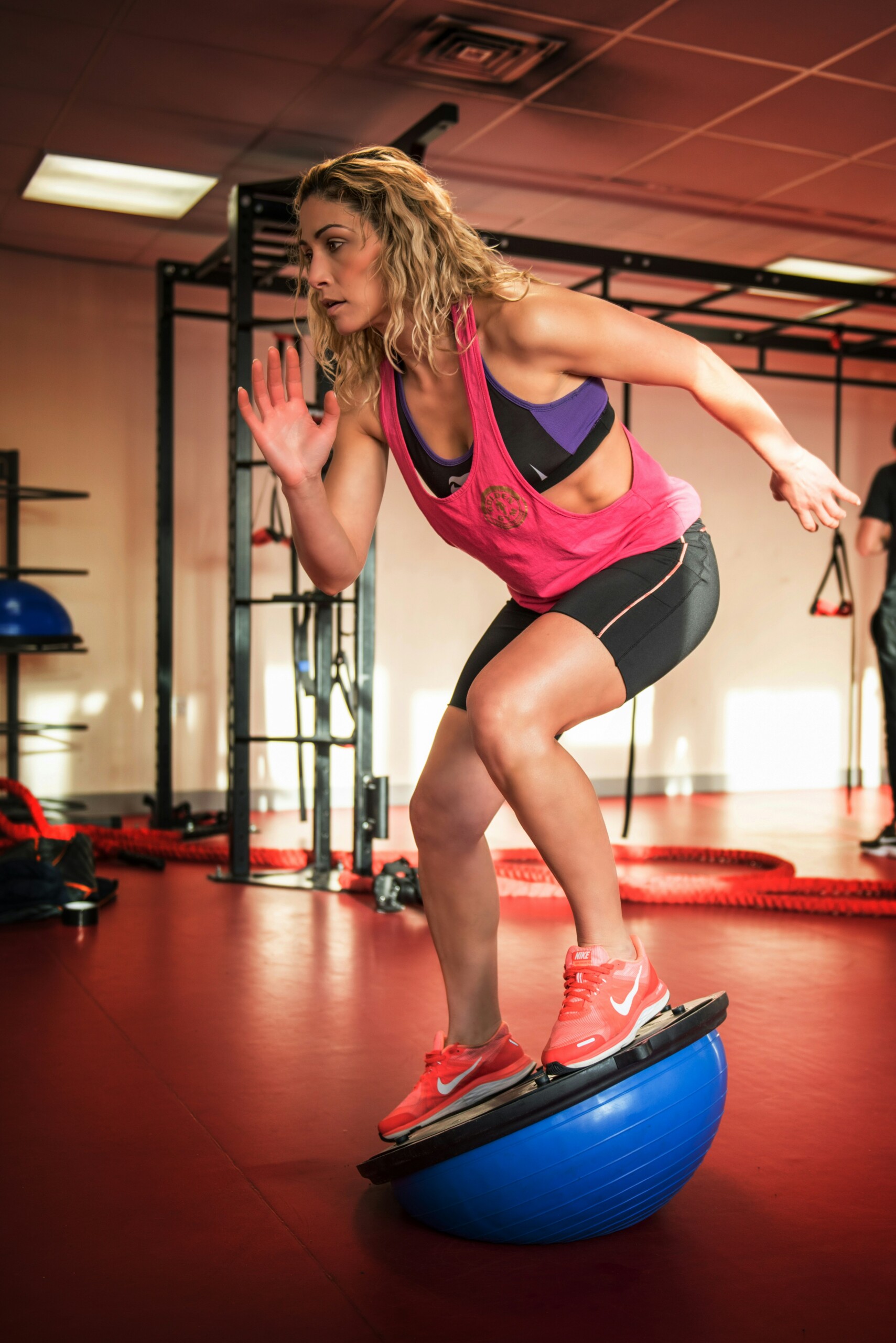 woman in fitness wear balancing on a half shaped blue ball at the gym