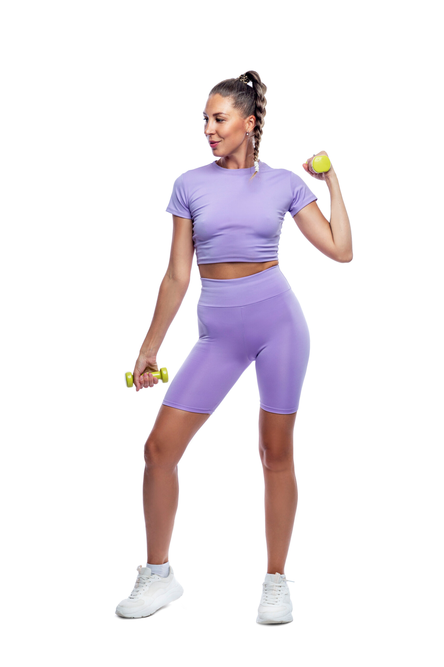 A slender young woman in purple sportswear with dumbbells does exercises. Sports, energy and health. Isolated on white background. Full height. Vertical.