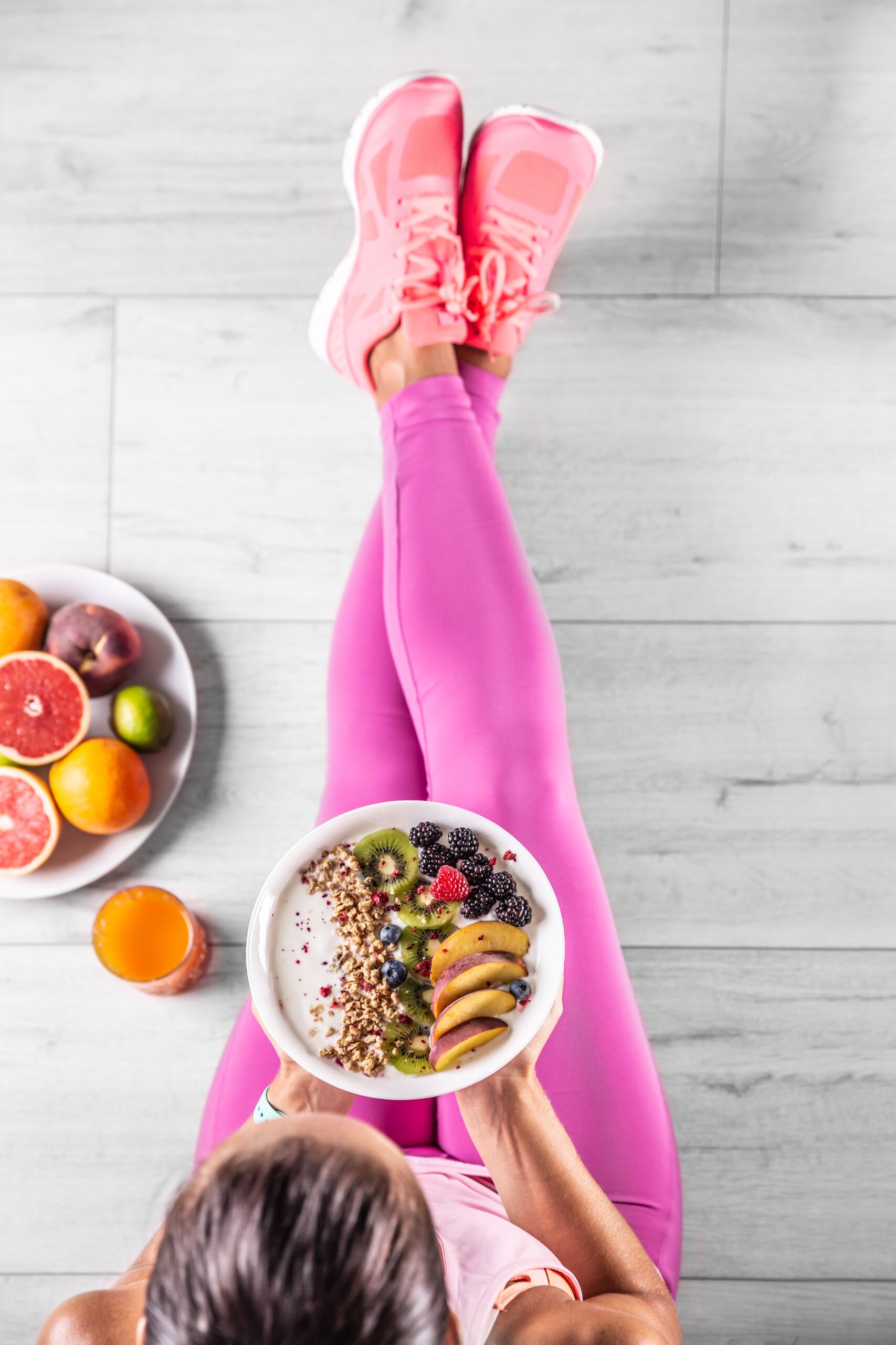 lady with pink leggings and orange sneakers eating a healthy salad and plate of fruit beside her