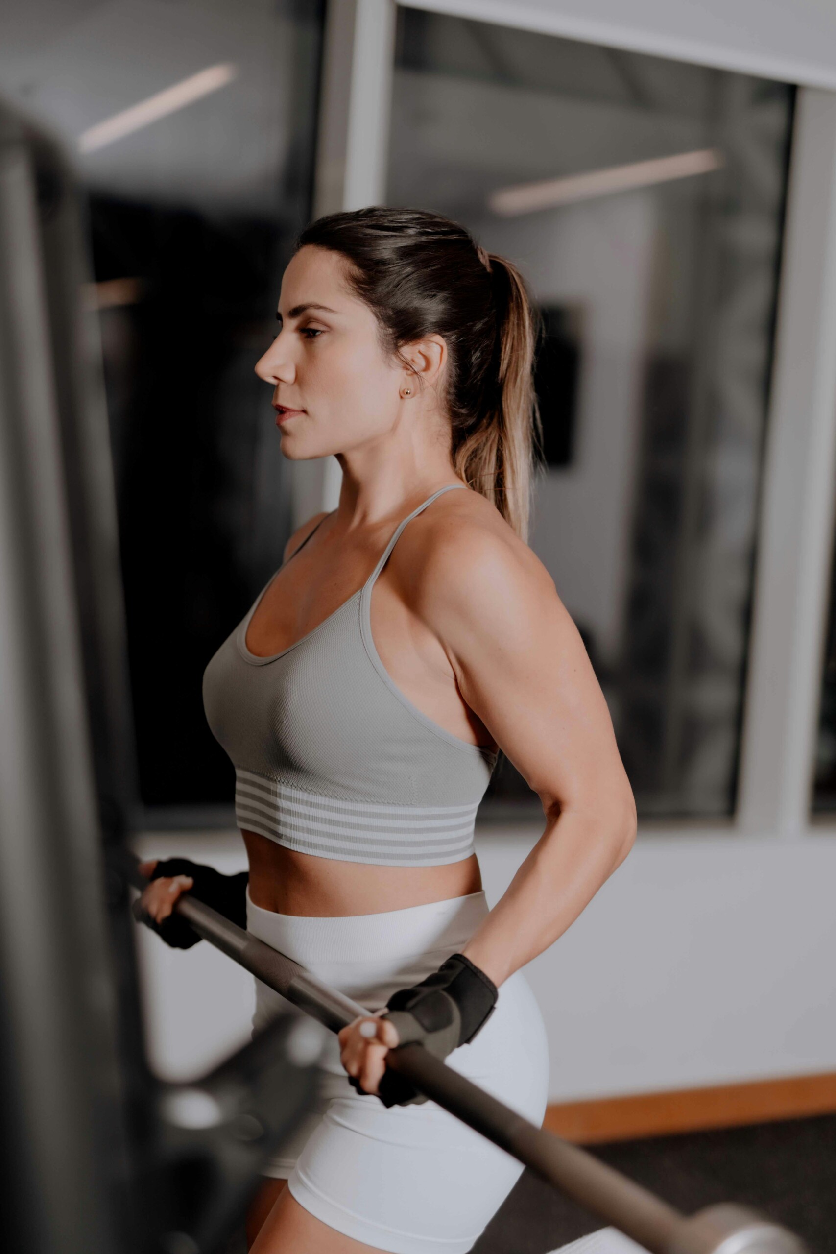 woman in grey sports bra and bike shorts with black gloves curling a barbell