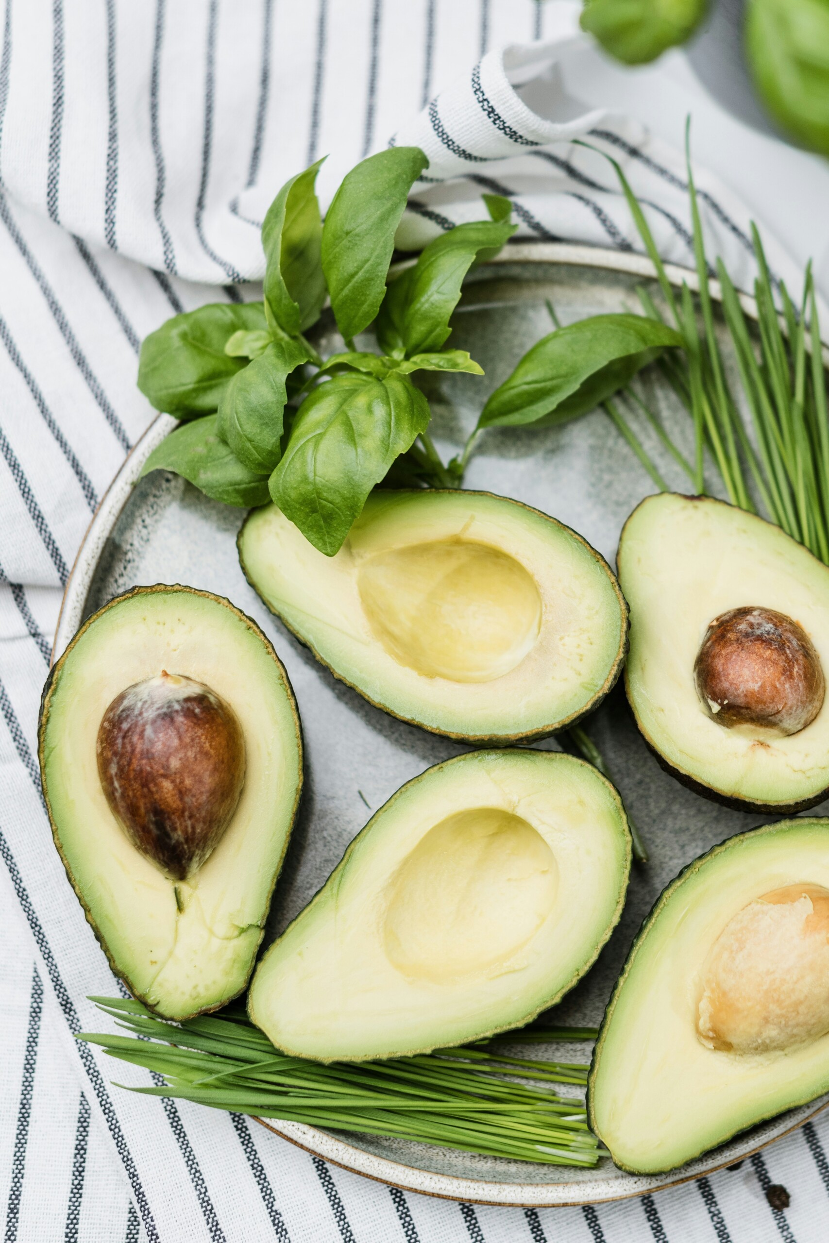 Fresh avocados sliced in half on a ceramic plate with basil and chives, representing healthy fats and superfoods for everyday wellness.