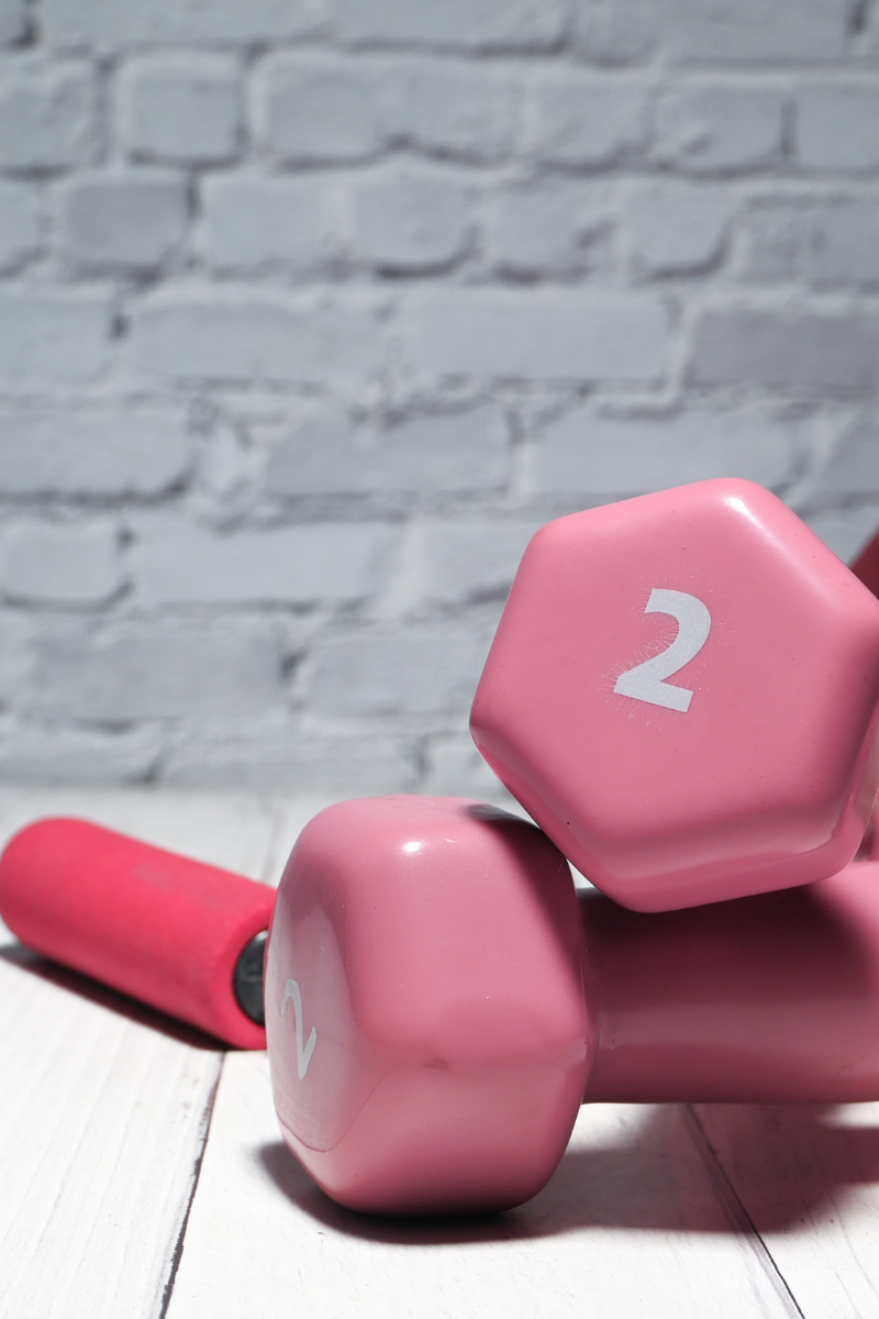 Pink dumbbells and resistance handle on a wooden surface representing strength training and muscle building for women