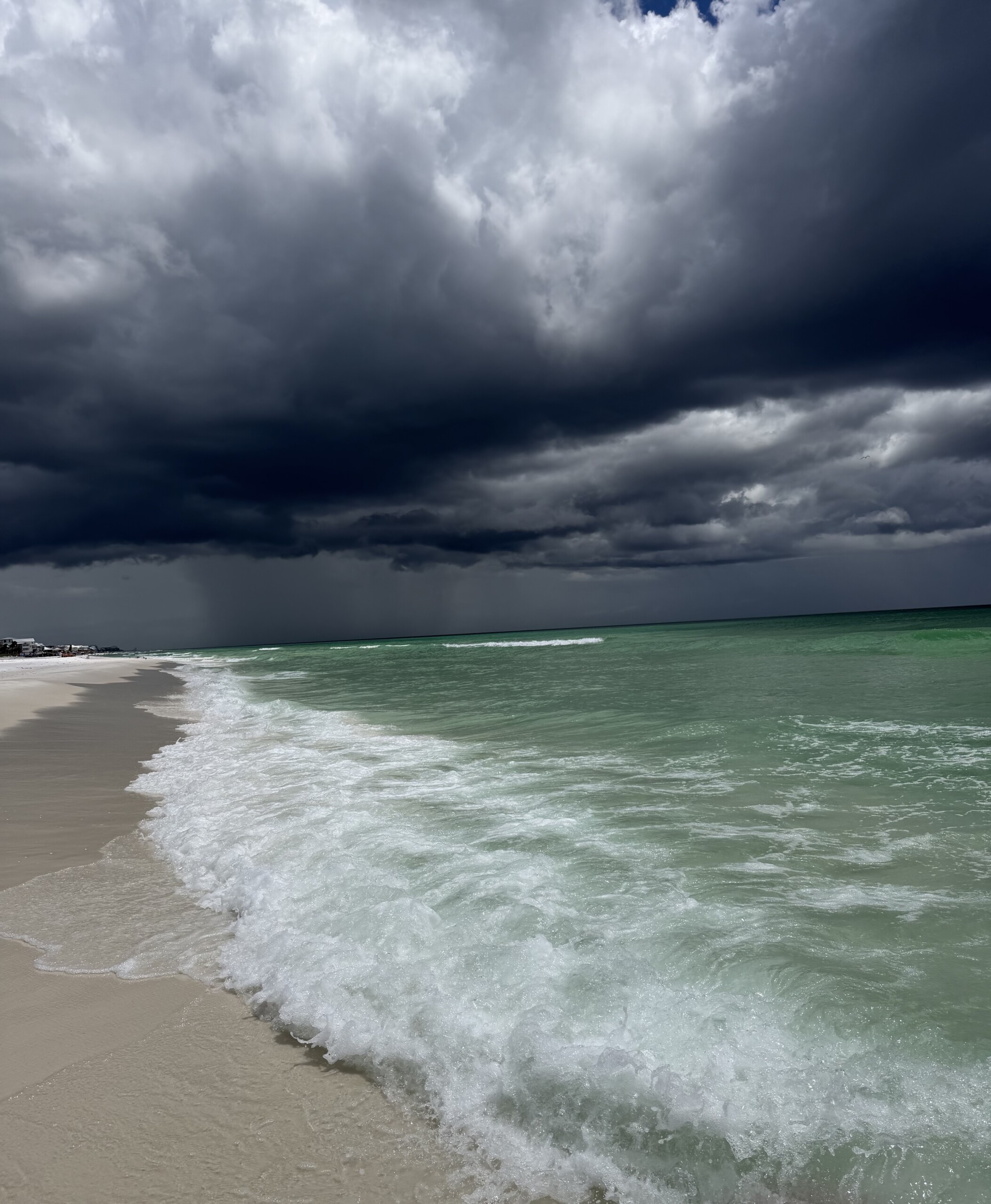 Dark storm clouds rolling over a turquoise ocean and sandy beach.