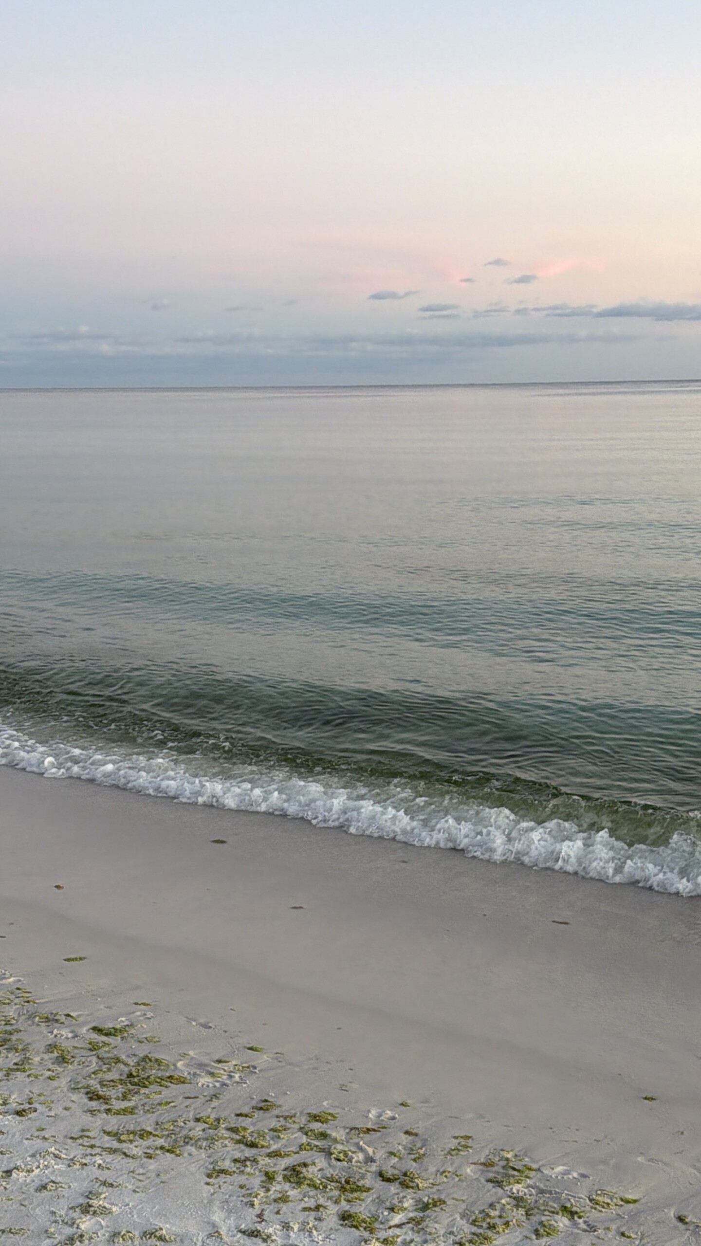 Gentle ocean waves washing onto a sandy beach beneath a soft pink and blue sky, reflecting God's words about the boundaries of the sea in Job 38:11.
